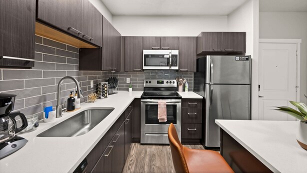 A modern kitchen with dark wooden cabinets, stainless steel appliances, and a white countertop.