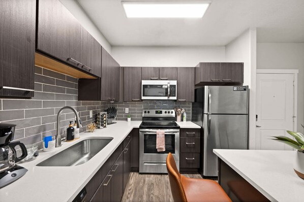 A modern kitchen with dark wooden cabinets, stainless steel appliances, and a white countertop.