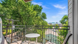 A balcony with a table and chairs, overlooking a green area with trees and buildings.