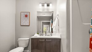 A bathroom with a toilet, vanity, sink, and shower curtain.