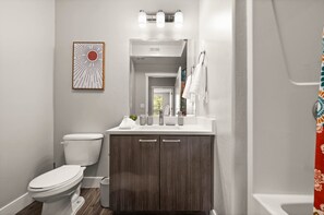 A bathroom with a toilet, vanity, sink, and shower curtain.