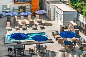 Area piscina sul tetto con poltronne da relax e ombrelloni, un barbecue e un muro in pietra.