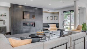 Un salon moderne avec un canapé d’angle, deux fauteuils, une table basse et un téléviseur à écran plat fixé à un mur de couleur sombre.