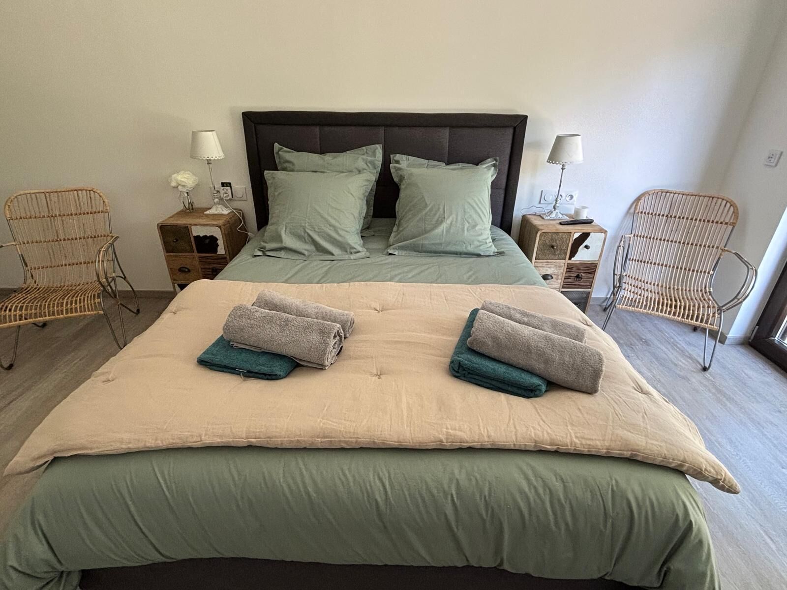 Una cama doble con dos almohadas, una mesita de noche con lámpara y dos sillones de mimbre.