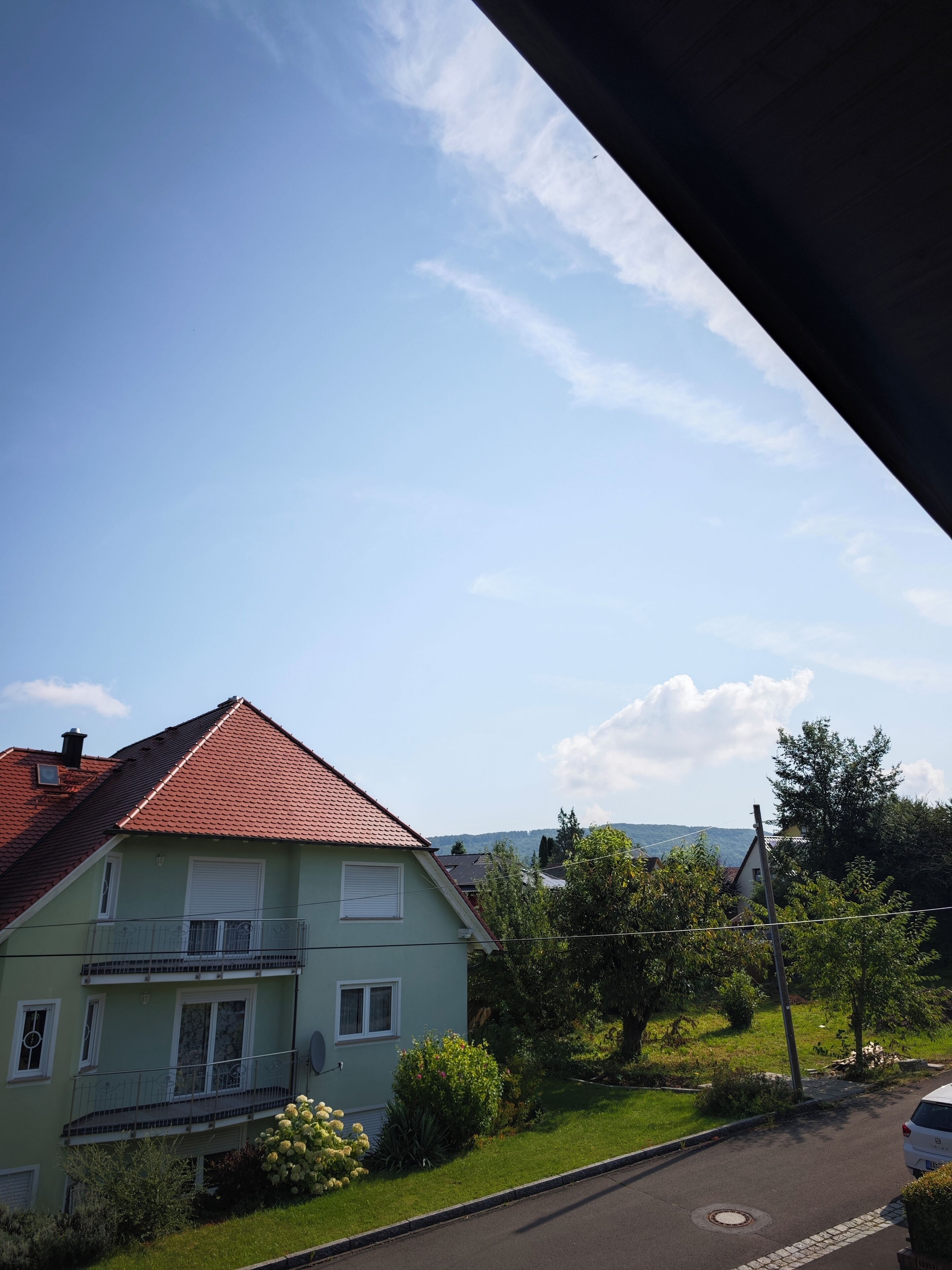 Ein Wohngebäude mit rotem Ziegeldach, einem Balkon und einem gepflegten Garten.