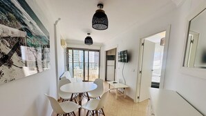 Eine moderne Küche mit weißen Schränken, ein Essbereich mit einem runden Tisch und Stühlen sowie ein großes Fenster mit Blick auf die Stadt.