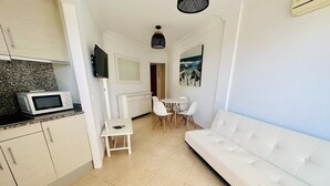 Ein kompakter Wohnraum mit Küchenzeile, einem weißen Sofa, einem Esstisch mit Stühlen und einem Bild an der Wand.