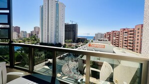 Un balcón con vista a un paisaje urbano, que incluye edificios altos y el letrero de un supermercado.