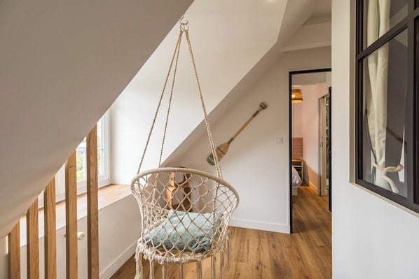 A macramé hanging chair in a spacious room with wooden floors and a sloped ceiling.