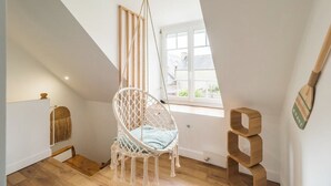 A cozy loft bedroom with a hanging chair, a small wooden shelf, and a window with a view of the outside. - Charming House on Loguivy de la Mer harbor (Ploubazlanec)