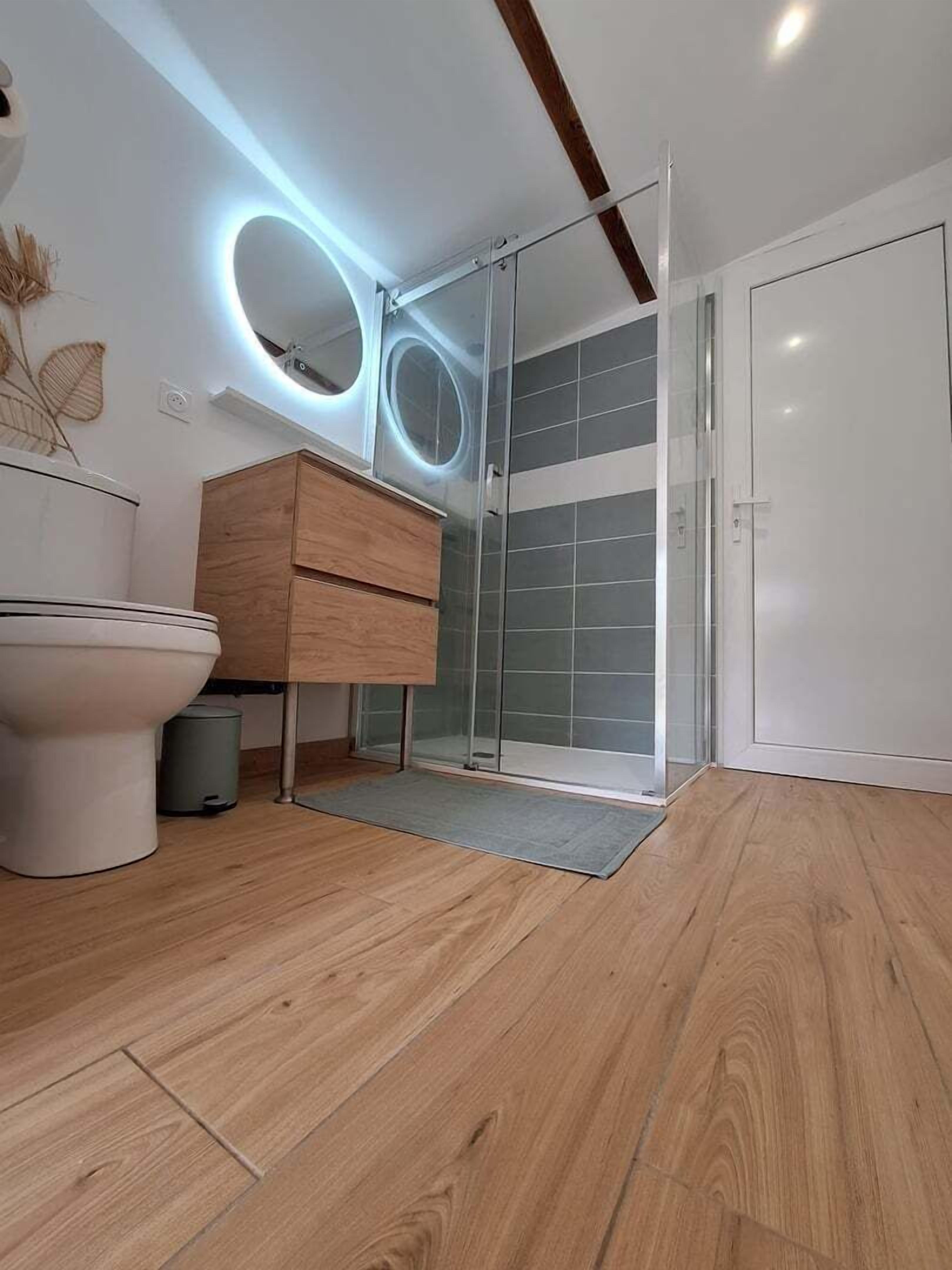 Ein modernes Badezimmer mit Holzboden, Toilette, Holzschrank und Duschkabine aus Glas.