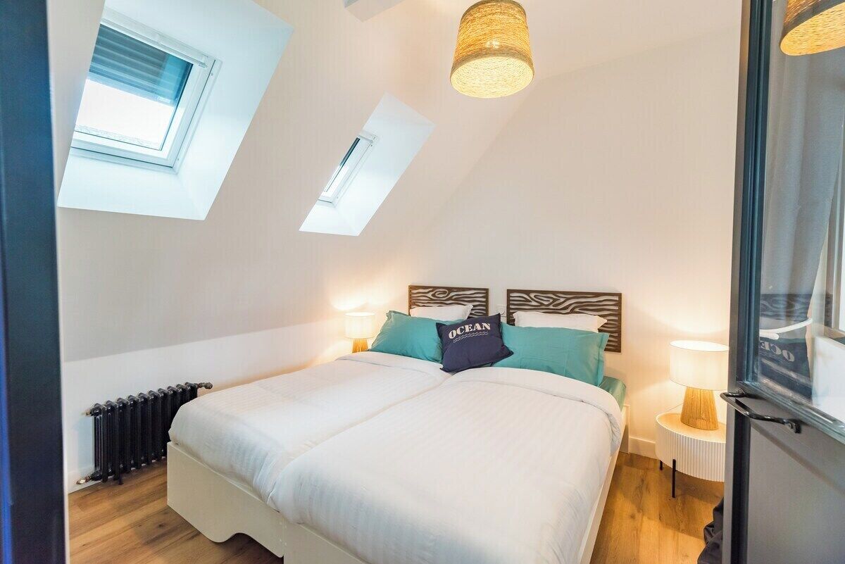 Ein Schlafzimmer mit Oberlicht, einem Bett mit weißer Bettwäsche, türkisfarbenen Kissen und einem Kopfteil mit Zeprazebramuster.