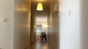 A hallway with wooden flooring, a hanging light fixture, and a door at the end.