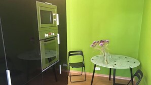A compact kitchen with a built-in oven and microwave, a round table with chairs, and a vase with flowers.