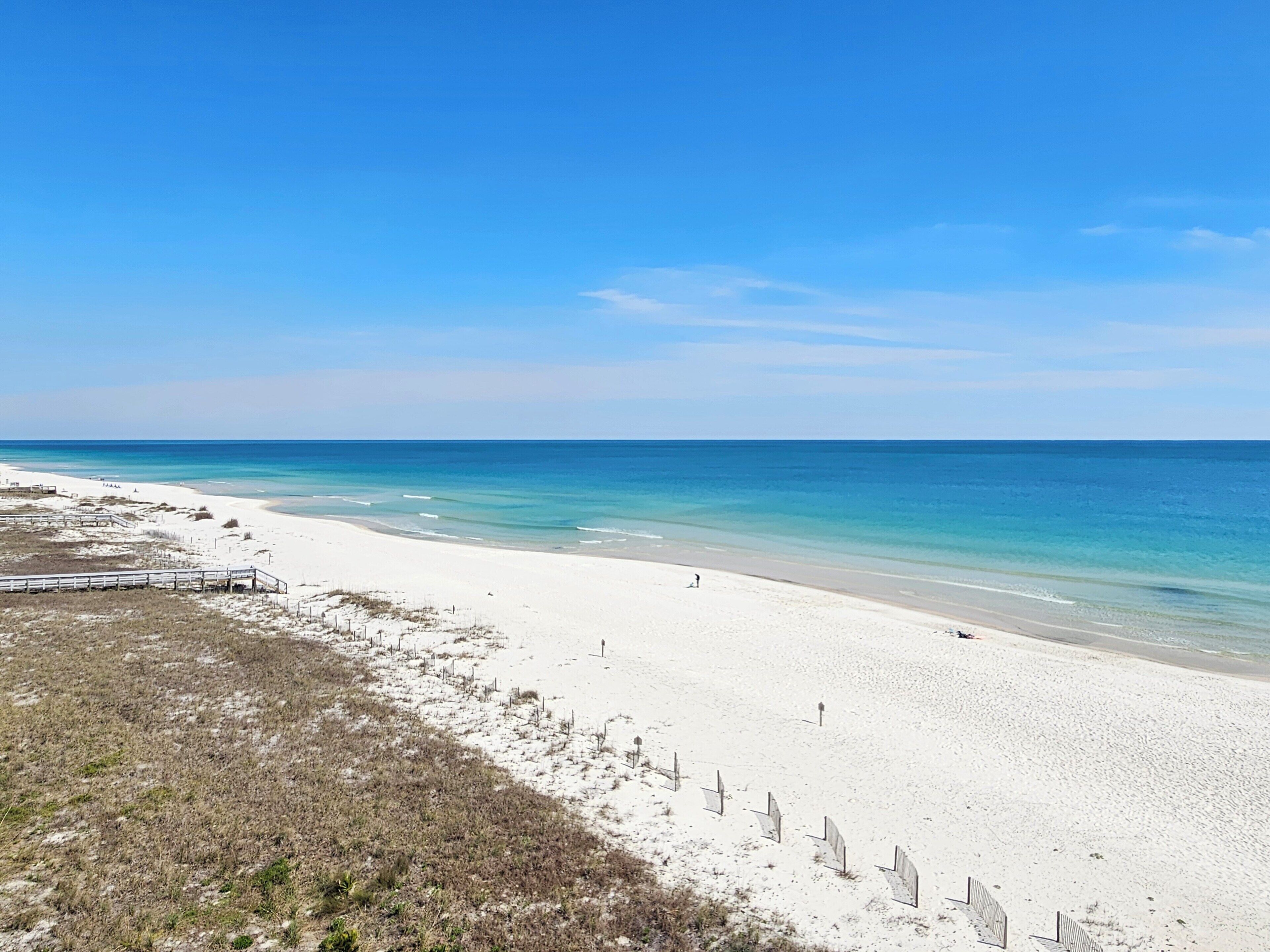A beach with white sand, a clear blue sky, and calm ocean waters.