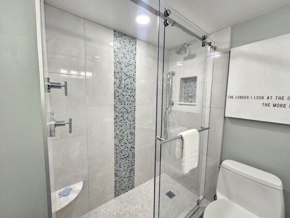 A modern bathroom with a glass-enclosed shower, a toilet, and a sink.