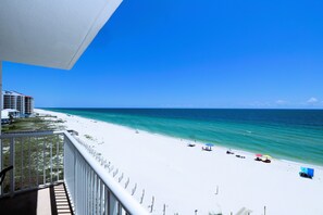 A beach view from a balcony with a clear sky, white sand, and turquoise water.