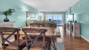 Amplia sala de estar con una mesa y sillas de madera, un conjunto de sofás y vistas al exterior.