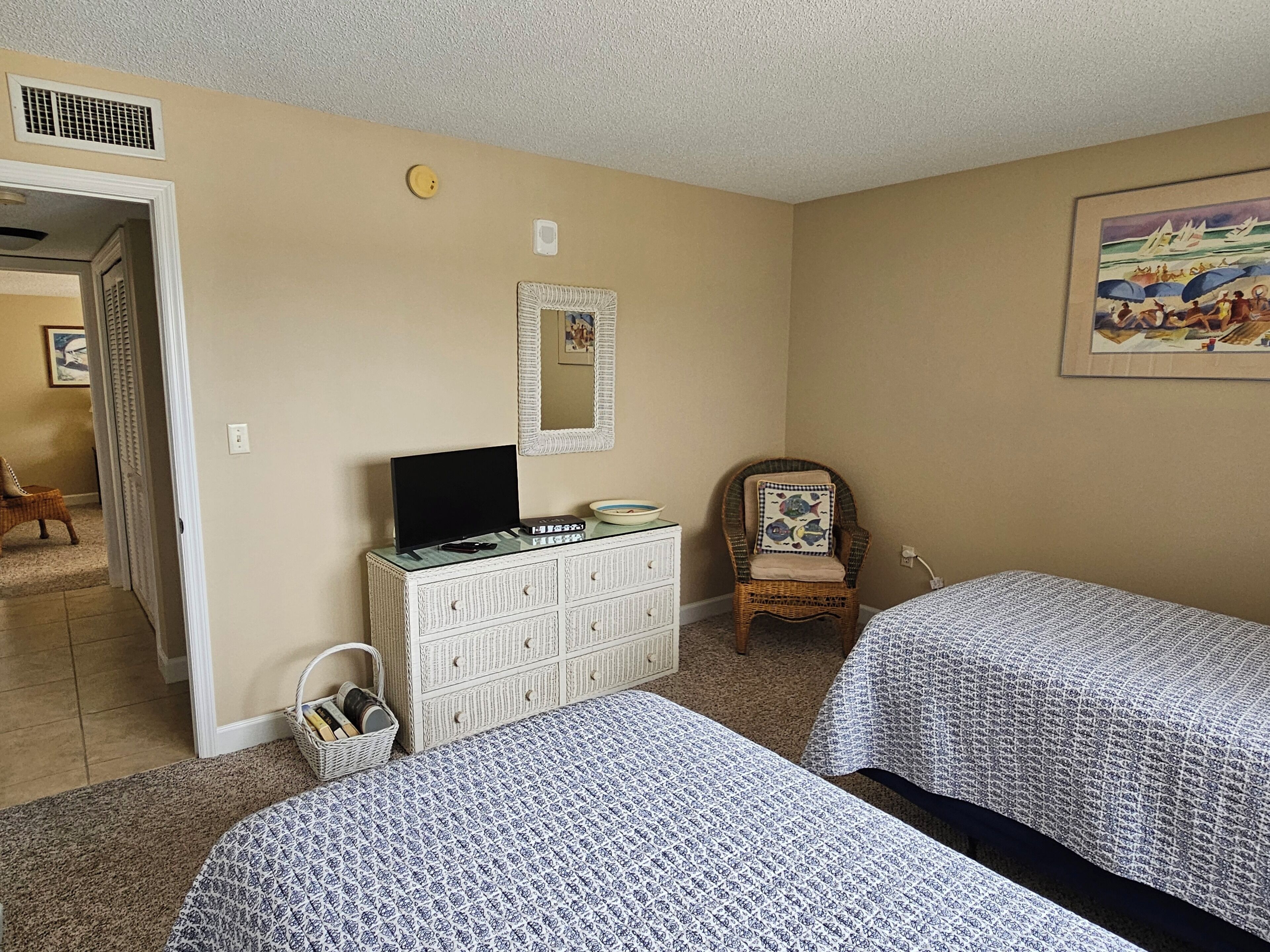 A bedroom with two beds, a dresser, a chair, a painting, and a door leading to another room.