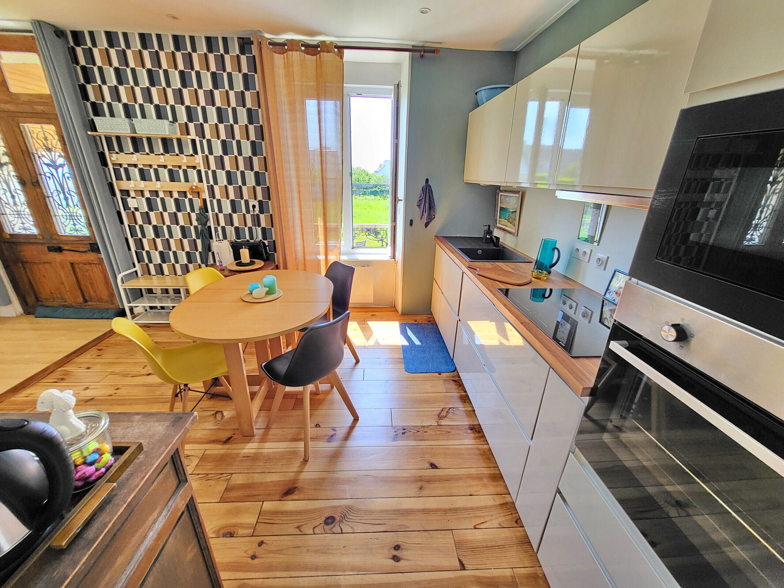 A modern kitchen with a built-in oven, a dining area with a round table and chairs, and a patterned wall.