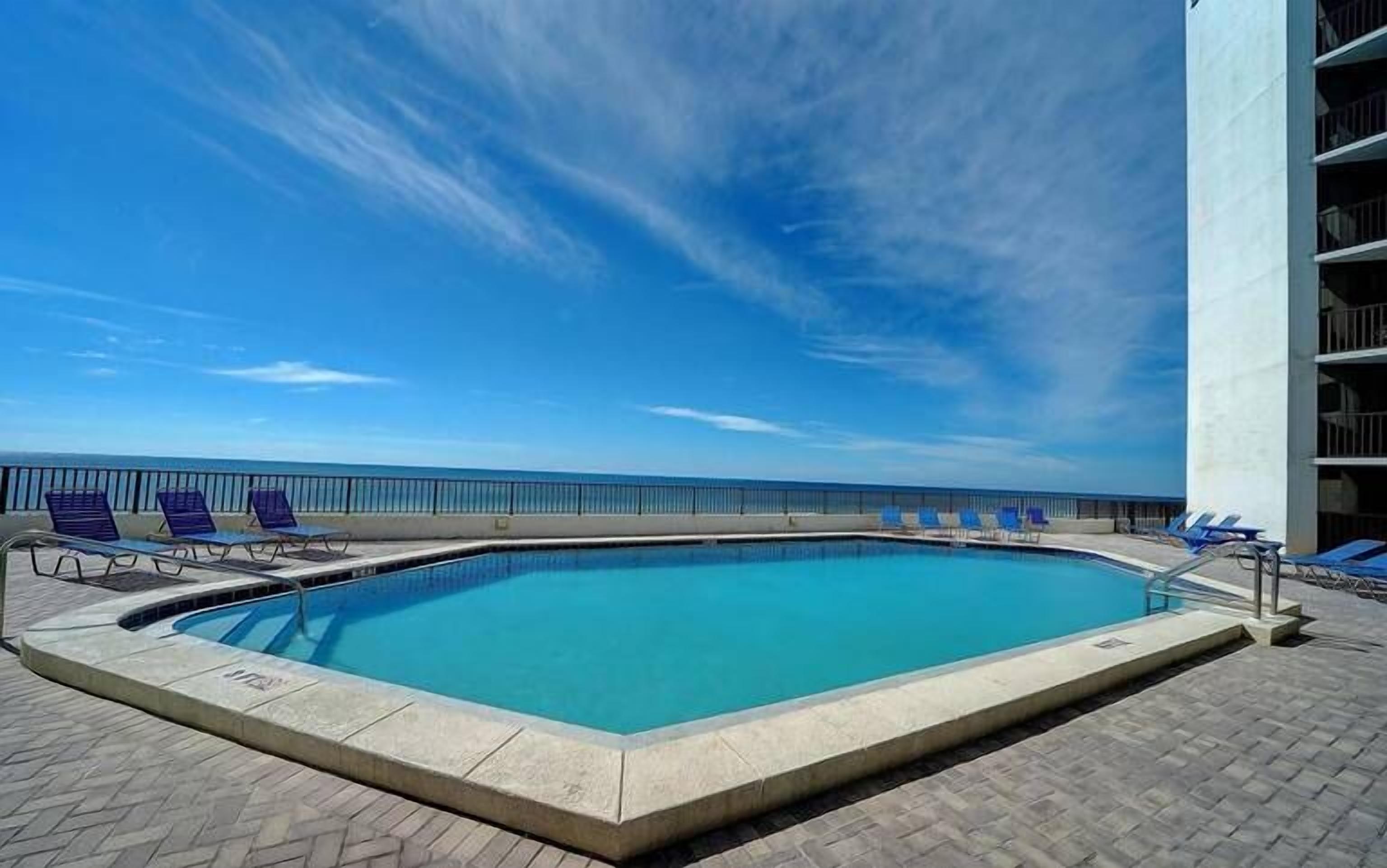 Une piscine avec vue sur l’océan, entourée de chaises longues et d’un bâtiment.