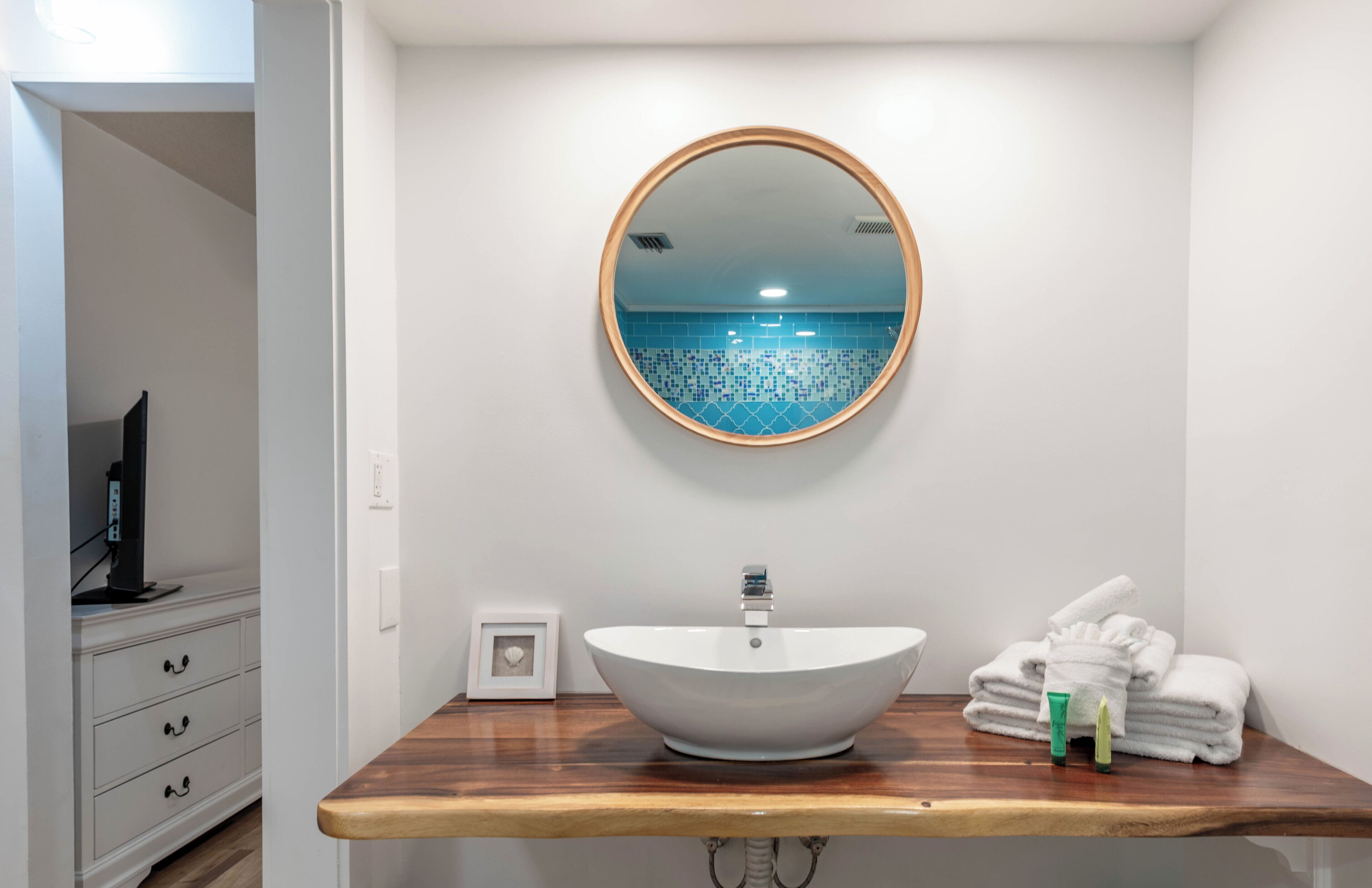 Un baño con un lavabo blanco tipo tazón, un espejo redondo y una encimera de madera.