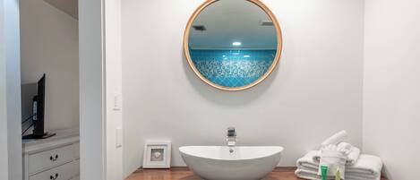 Un baño con un lavabo blanco tipo tazón, un espejo redondo y una encimera de madera.