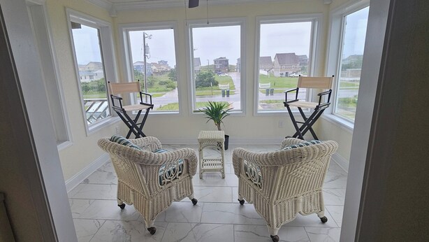 A room with two wicker chairs and a small table, large windows with a view of a residential area.