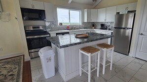 A modern kitchen with white cabinets, stainless steel appliances, a large island with stools, and a view through the window.