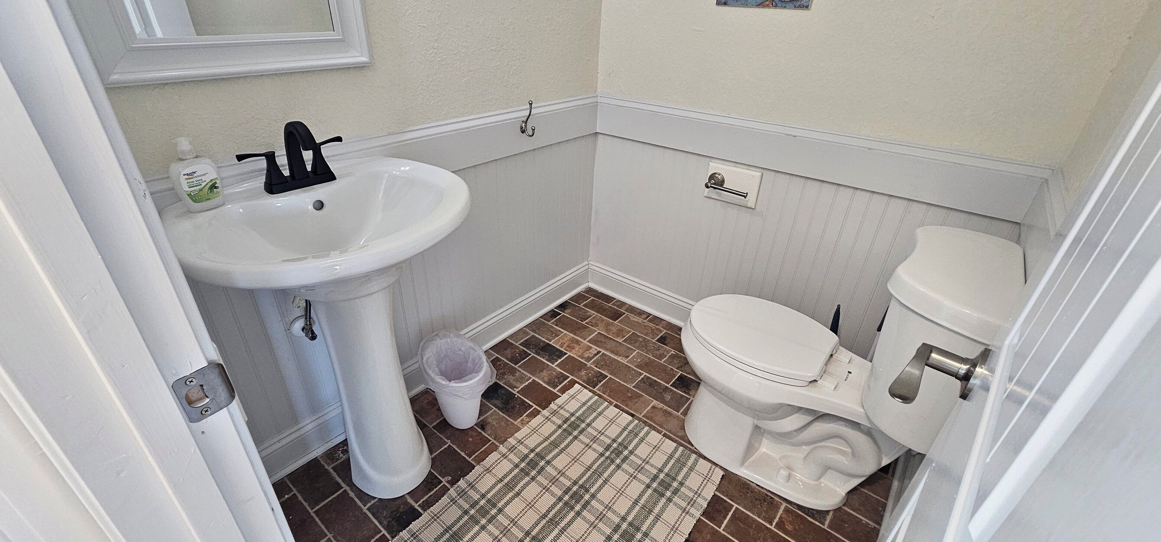 Un bagno con lavandino, water e cestino bianchi.