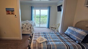 A bedroom with two beds, a dresser, a chair, and a balcony with a view.