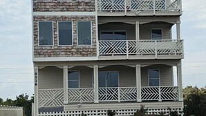 A two-story building with a balcony on each floor, a white picket fence, and a landscaped garden area.