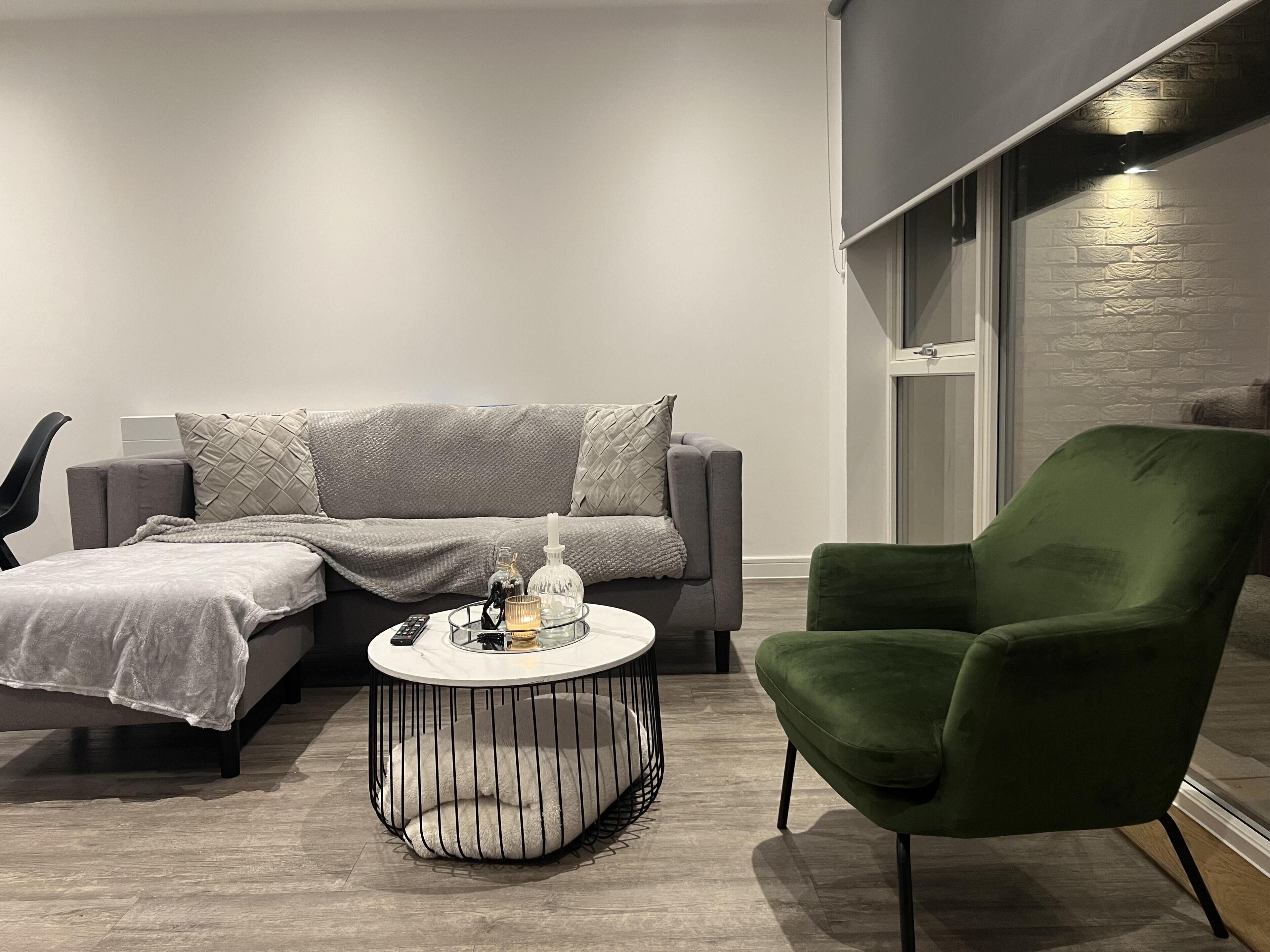 A modern living room with a grey sofa, a green armchair, and a round coffee table with a glass top.