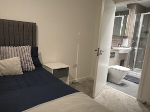 A bedroom with a bed, bedside table, and a bathroom visible through an open door. - Riverside Retreat in Barking (Barking)