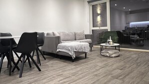 A modern living room with a sofa, chairs, a coffee table, and a glass door leading to a kitchen area. - Riverside Retreat in Barking (Barking)
