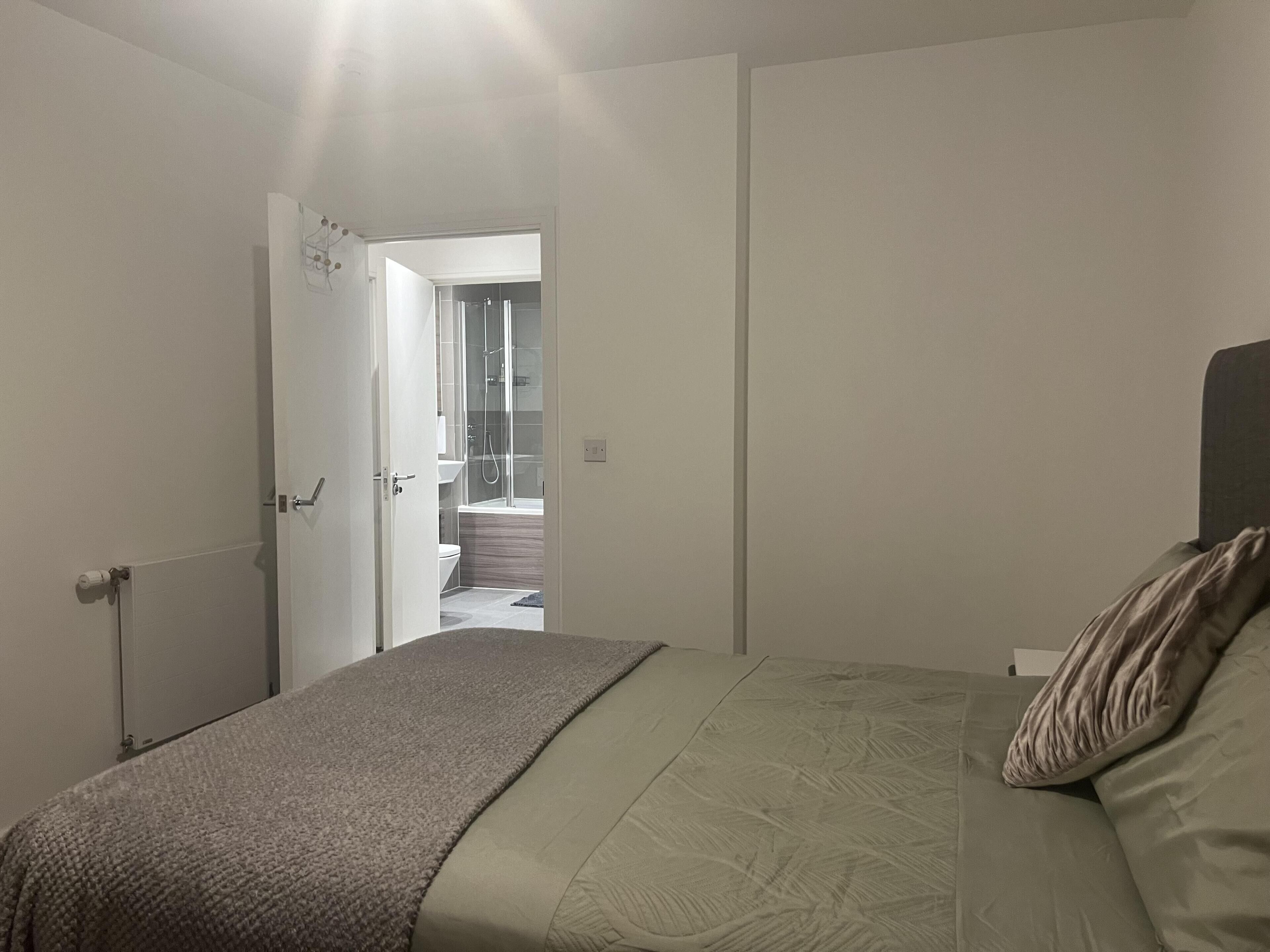 Een slaapkamer met een bed, een deur naar een badkamer en uitzicht op een douchegedeelte.