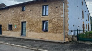 Un edificio de piedra de dos pisos, con techo plano, un pequeño porche y una valla de metal.