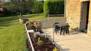 Un patio con pared de piedra, una mesa con sillas y un jardín con plantas.
