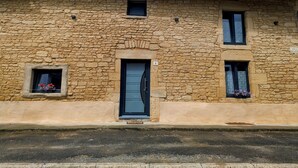 Un edificio de piedra con una puerta central, dos ventanas pequeñas con macetas de flores y un letrero sobre la puerta.