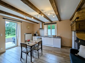A kitchen with wooden beams, a dining area with a table and chairs, and a view of the outdoors. - Charming Country Apartment with Modern Comfort, Terrace & Garden Views (Han-lès-Juvigny)