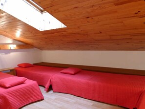 Une chambre avec deux lits, une lucarne et un plafond en bois.