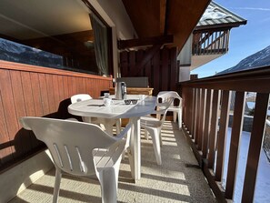 Varanda com mesa e cadeiras, cafeteira e vista para uma montanha nevada.
