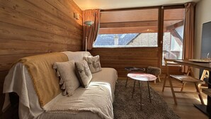 A cozy cabin room with a wooden interior, a sofa with cushions, a small round table, and a television.