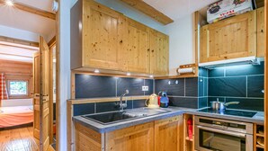 A compact kitchen with wooden cabinets, a black countertop, a sink, a kettle, and an oven. - Charming apartment with wifi, ski-in/ski-out in Val-d'Isère (Val-d'Isère)