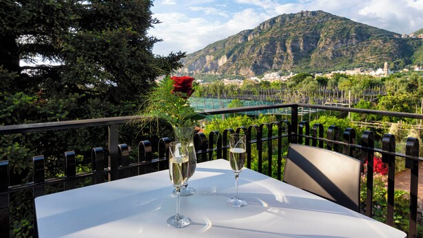 Une table avec deux coupes à champagne et une rose rouge, placée sur un balcon donnant sur un paysage montagneux.