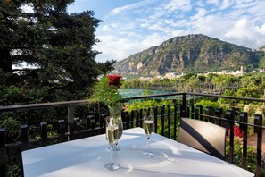 Een tafel met twee champagneglazen en een rode roos op een balkon met uitzicht op een bergachtig landschap.