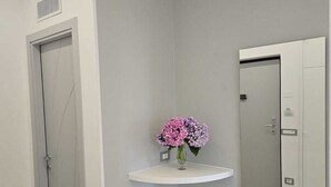 Un coin de pièce avec une porte blanche, un mur blanc et une étagère blanche sur laquelle est posé un vase de fleurs.
