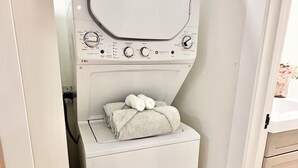Een compacte, witte wasmachine met een bovenin zitdeur, geplaatst in een smalle ruimte tussen twee deuren.