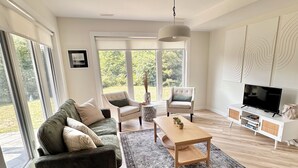 Een moderne woonkamer met een bank, fauteuils, een salontafel en een televisie.