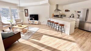 Een moderne woonkamer met een bank, salontafel en televisie. De keuken heeft een groot eiland met krukken, een magnetron en een koelkast.